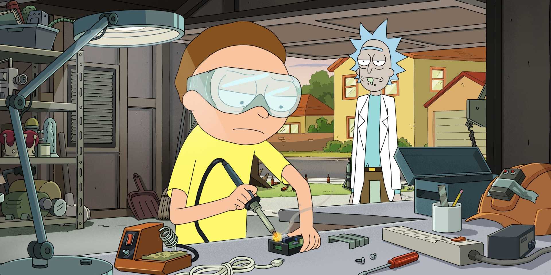 Morty, in a yellow shirt, sits in the garage welding as Rick stands in the doorway on Rick and Morty