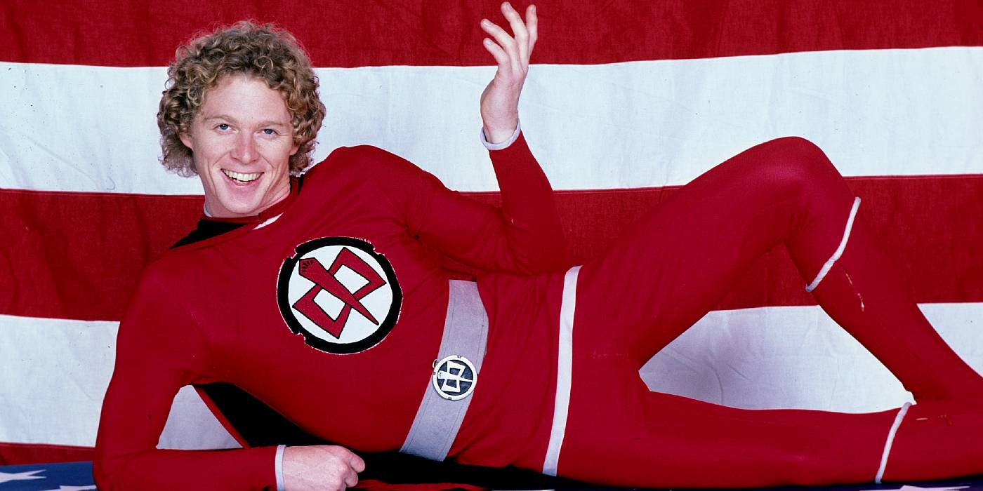 William Katt dressed in his superhero costume in front of a flag in The Greatest American Hero
